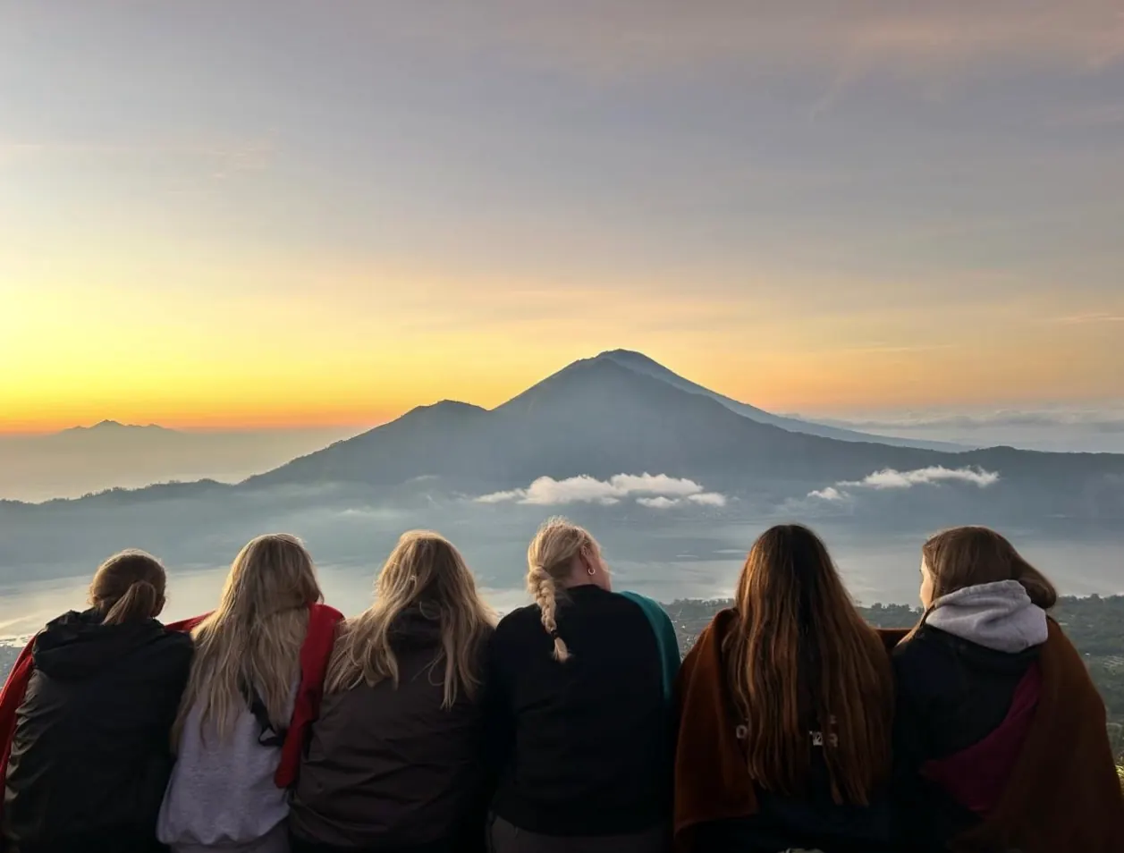 Five guests sitting side by side watching the sunrise over a volcano and a sea of cloud