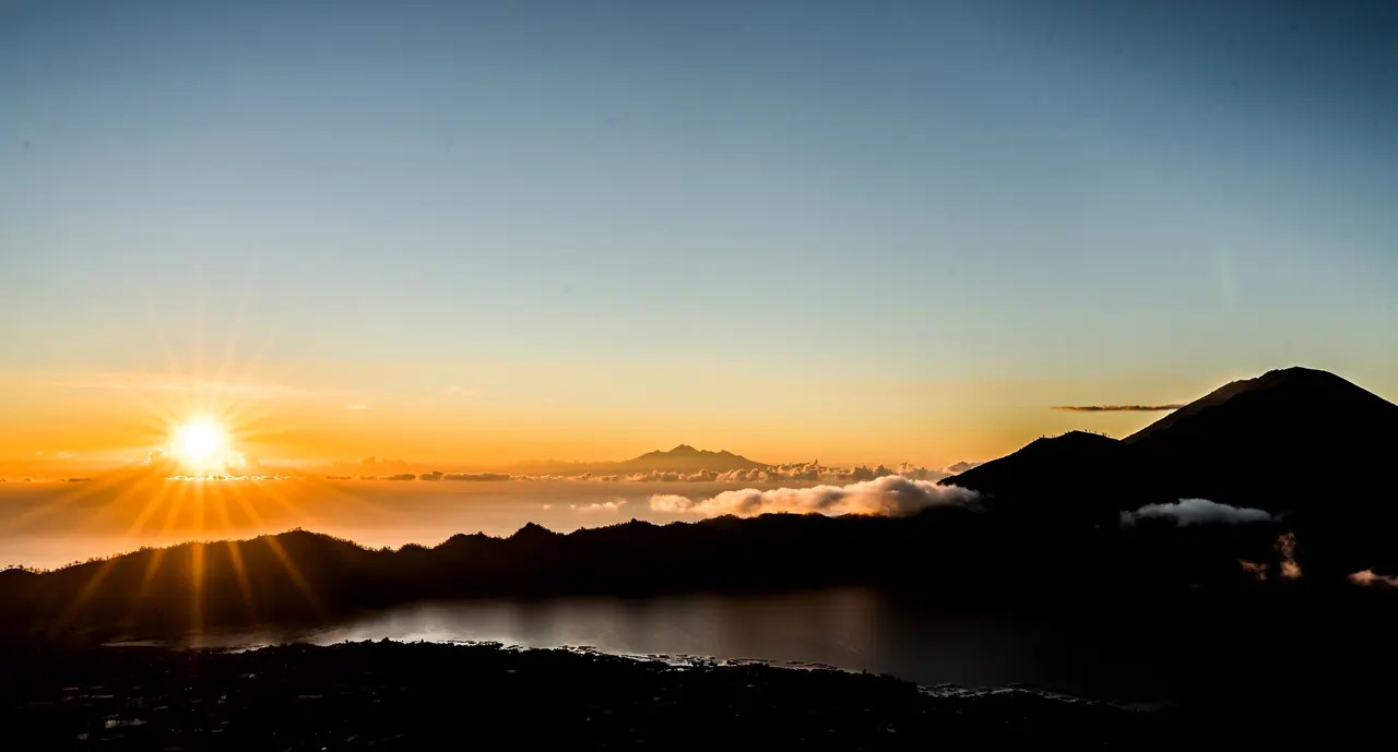 Sun rising over Mount Batur and its crater lake with cloud in the valley